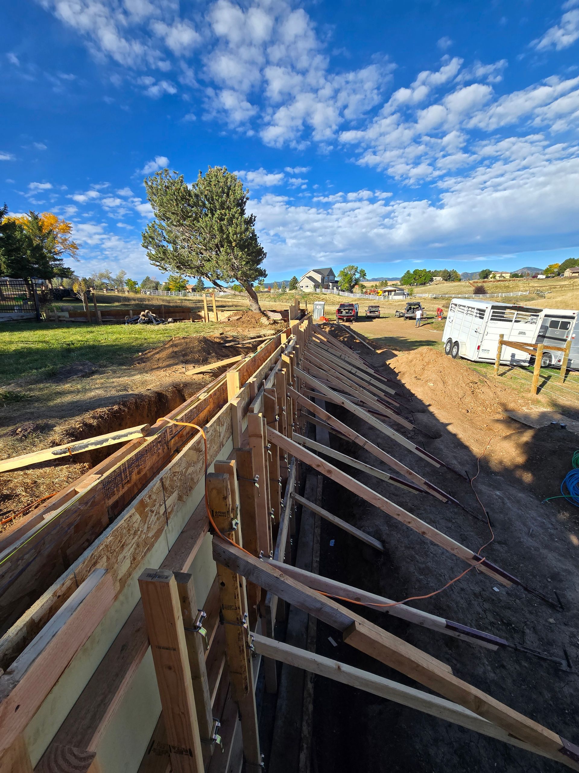 Wooden retaining wall under construction along a dirt road, with blue sky and clouds overhead.