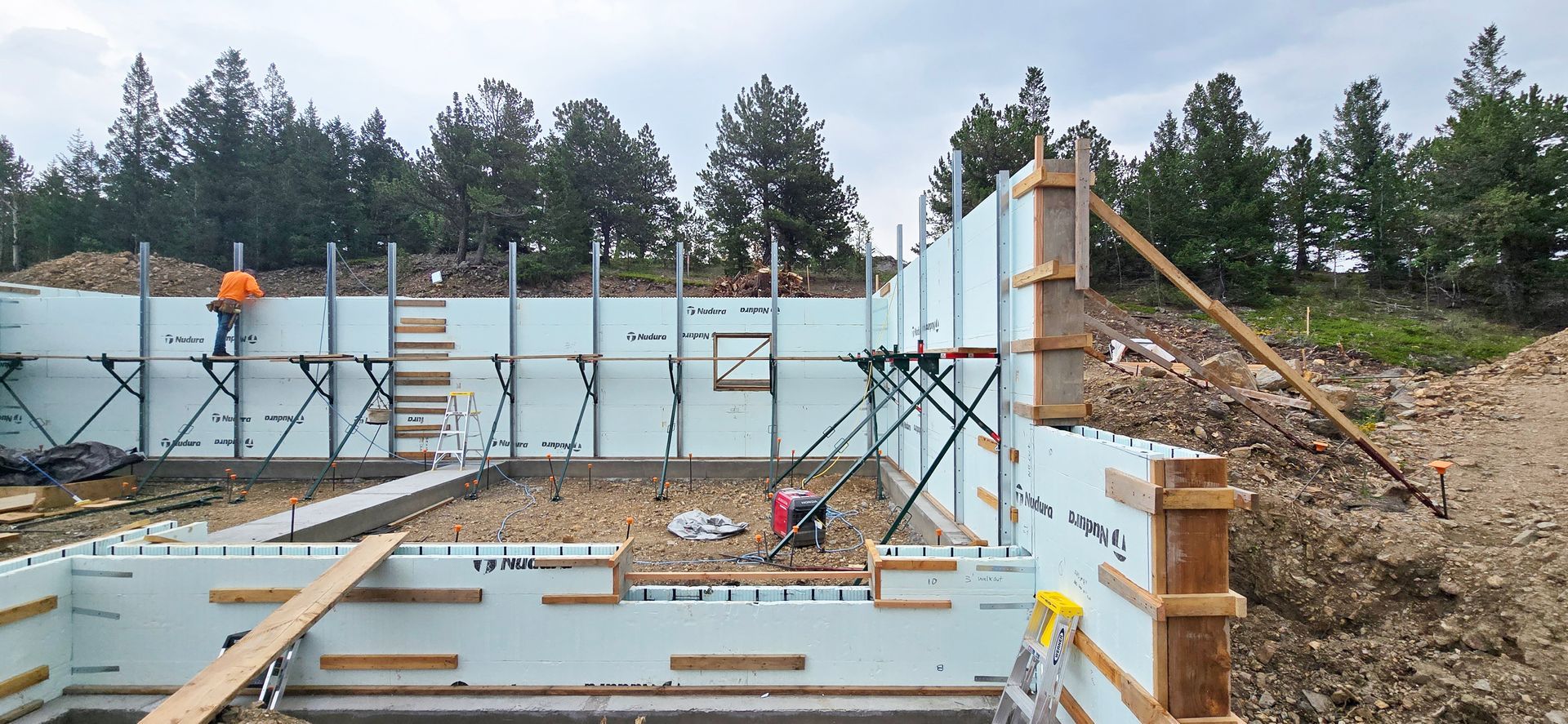 Foundation construction site with concrete walls, scaffolding, and workers under a cloudy sky