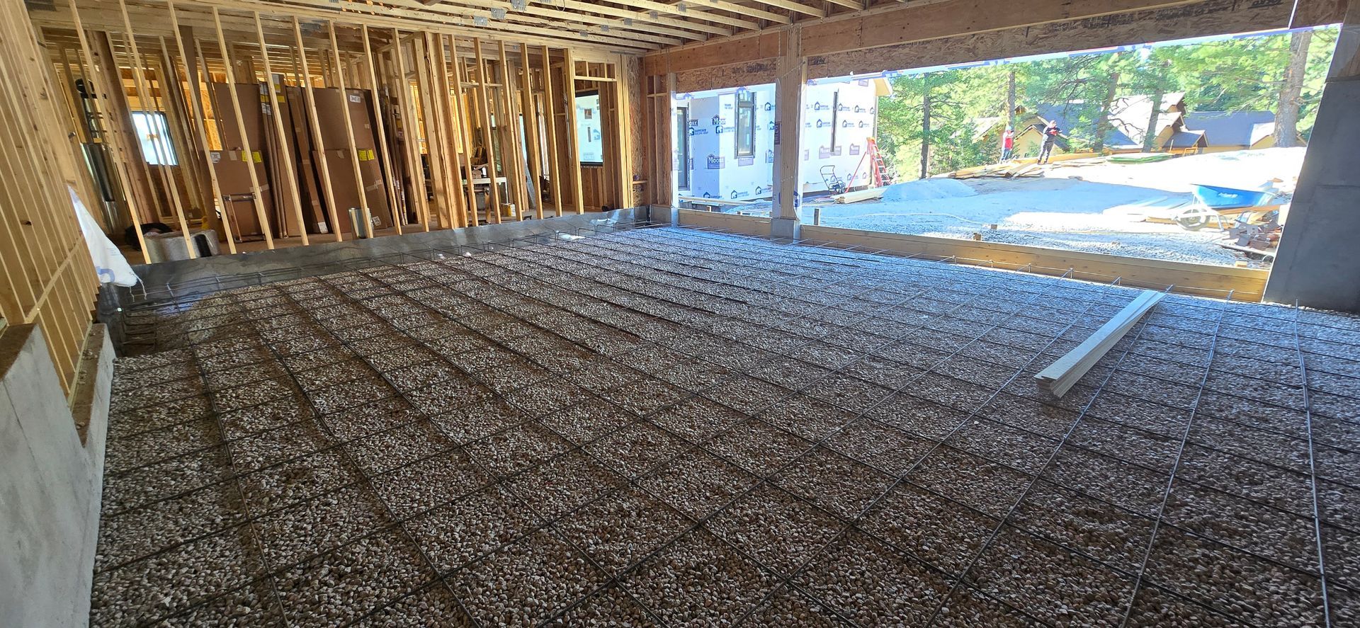 Gravel-covered construction floor inside a framed building, with open walls and bright light outside