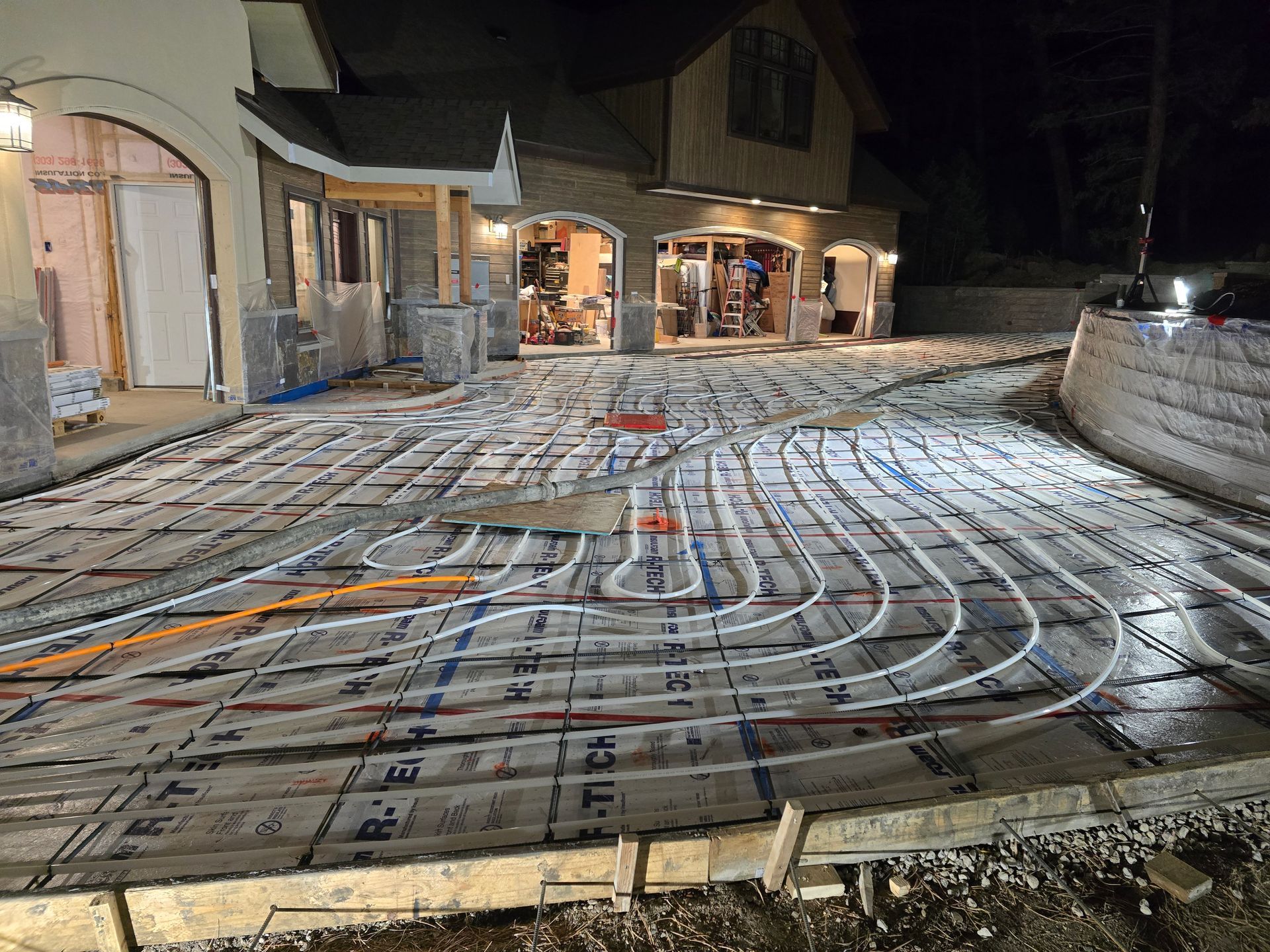 Nighttime construction site with underfloor heating pipes laid over insulation in a patio area.