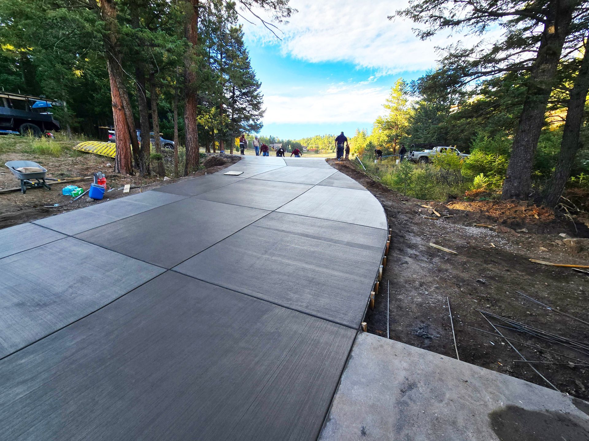Curved concrete path through a wooded park opening toward bright blue sky and water beyond