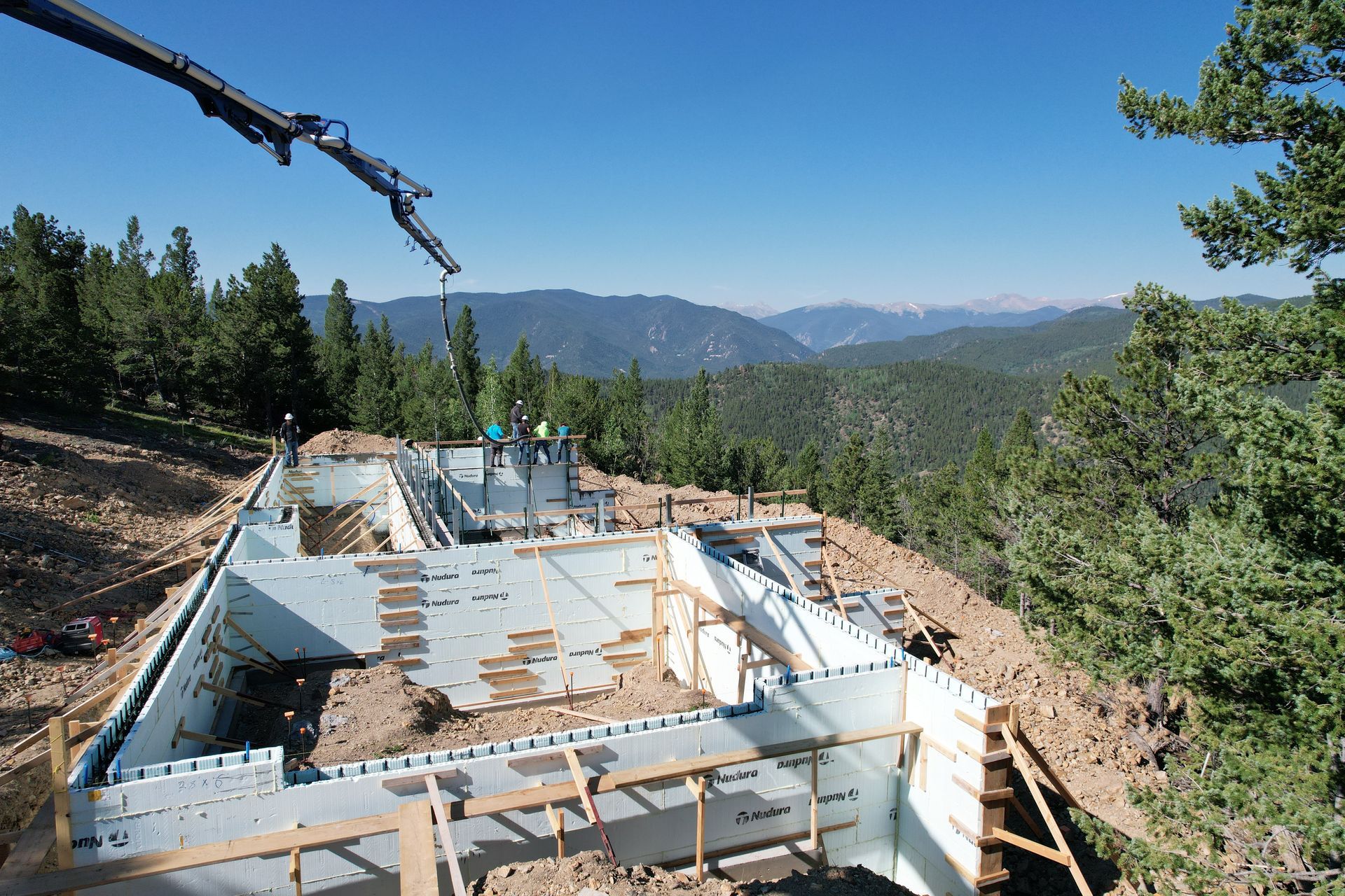 Partially built concrete house on a forested hillside with mountains in the background
