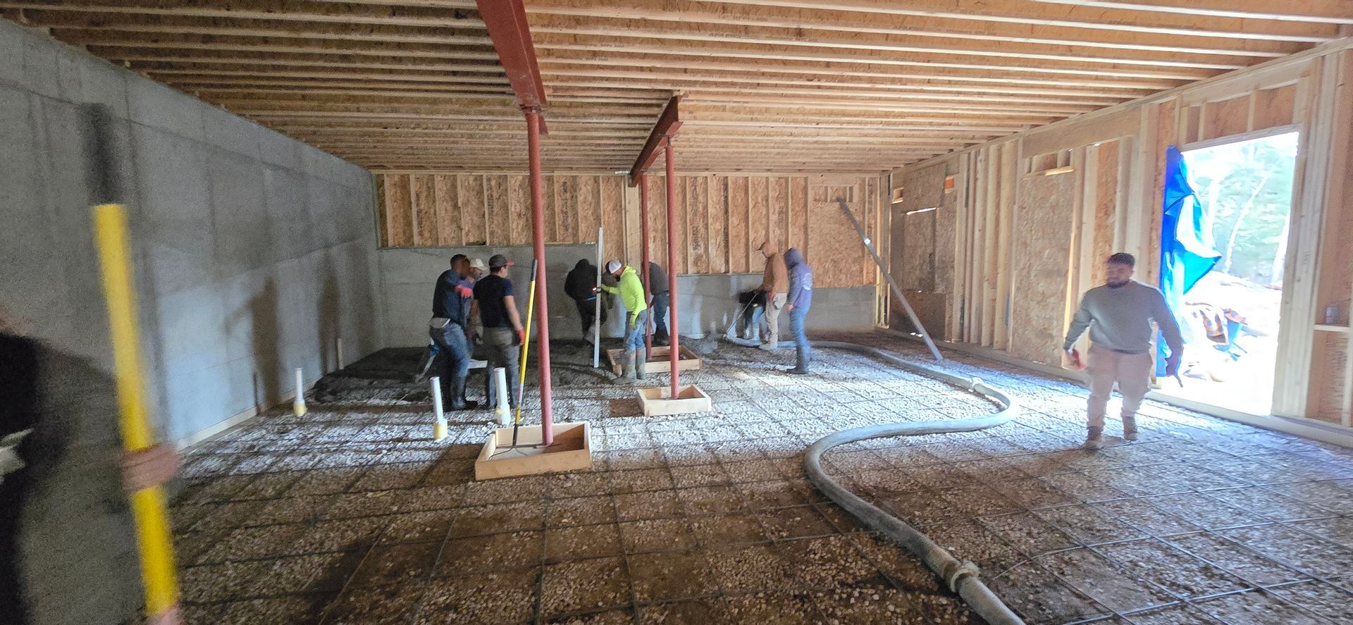Interior framing of a house under construction with workers and exposed wooden beams and wiring.