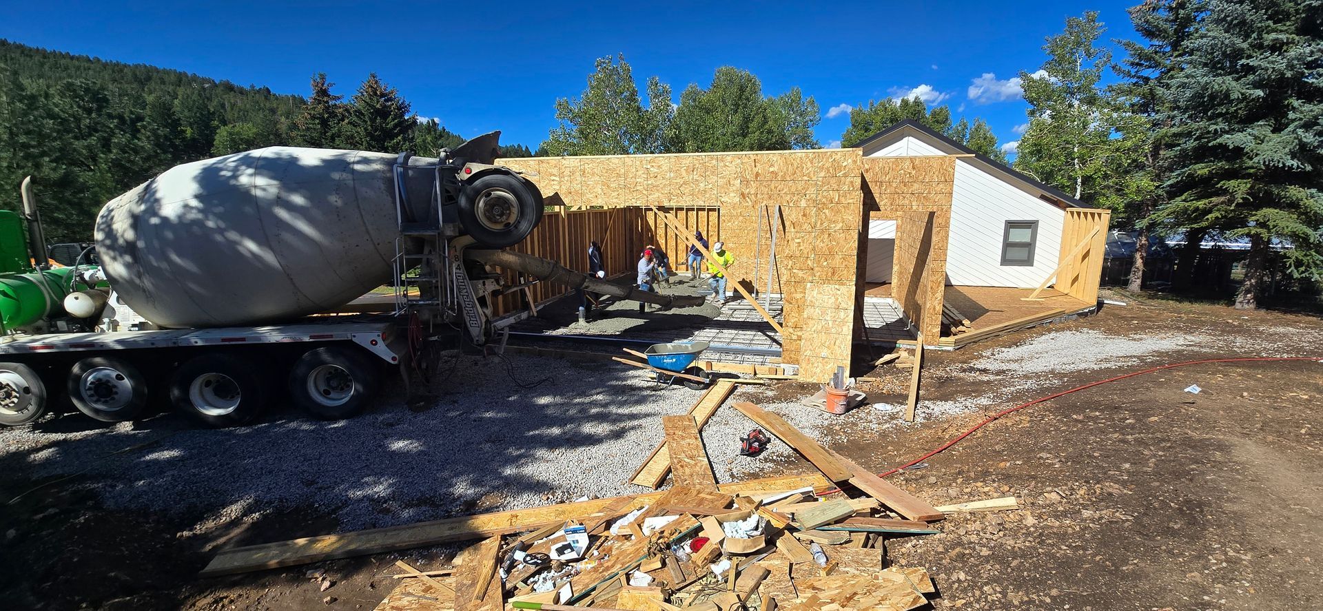 Construction truck with concrete mixer near a damaged building and scattered debris under a blue sky