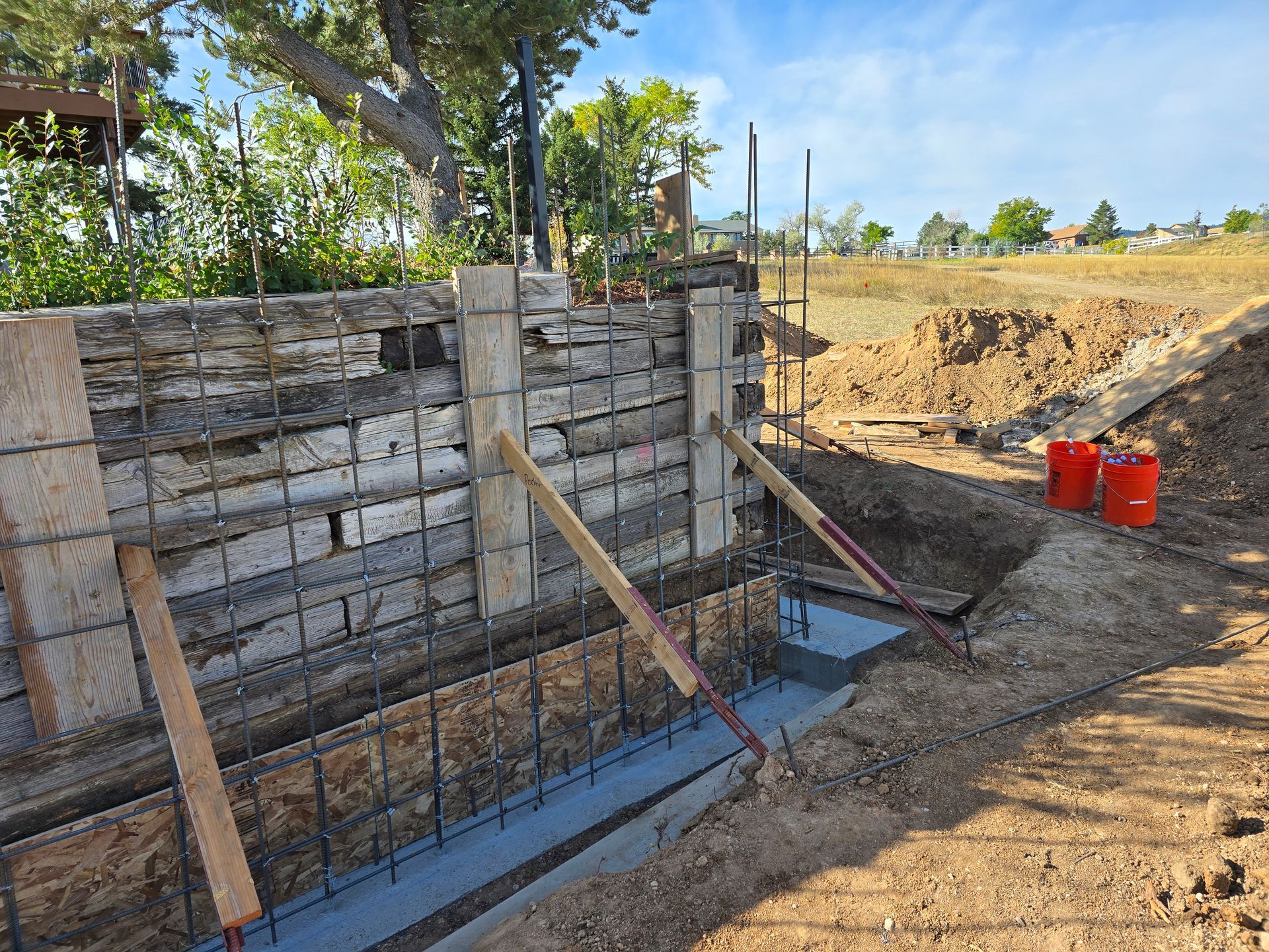 Construction site with a concrete foundation wall, rebar, wooden braces, and two red buckets