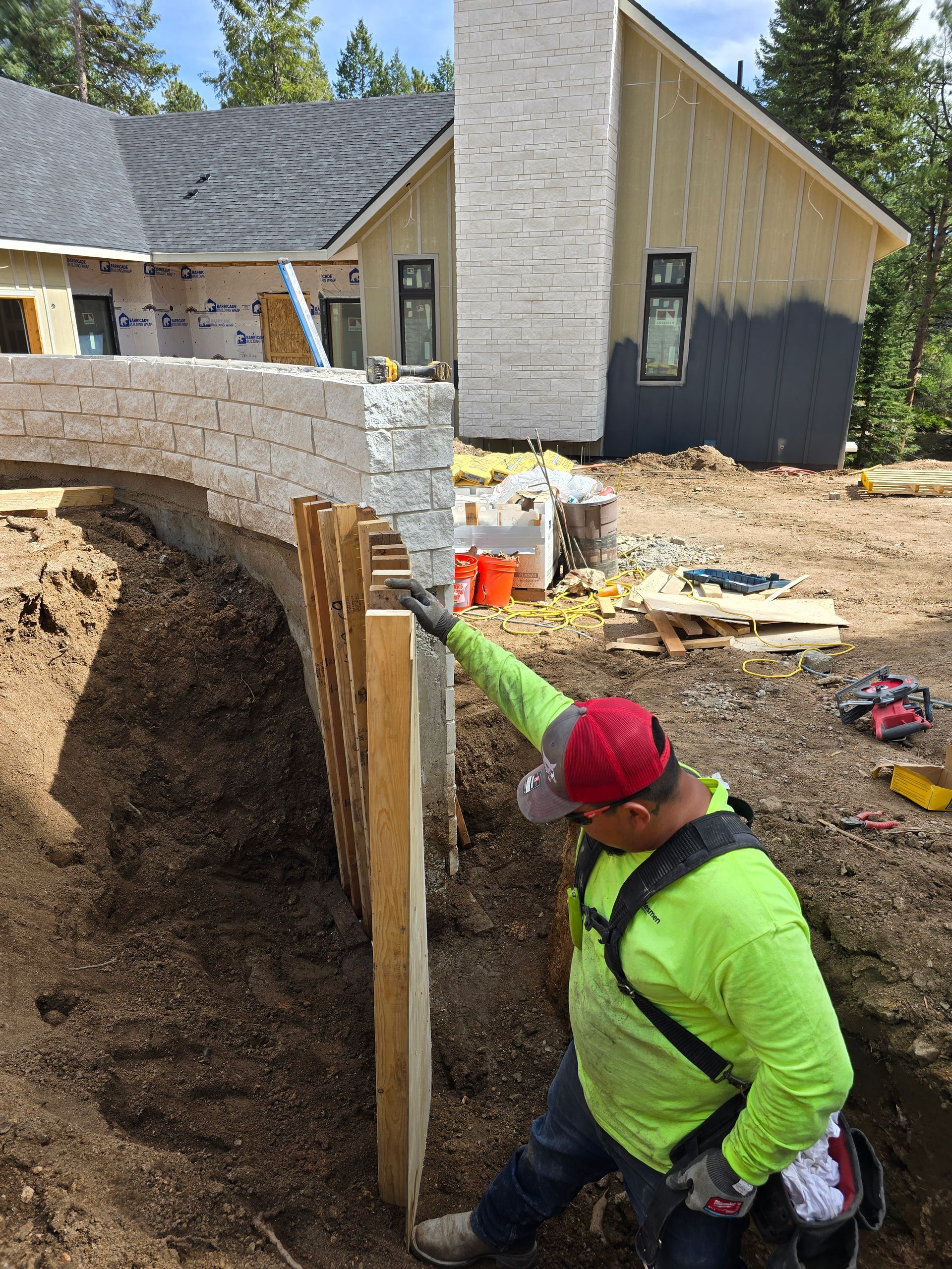 Worker in neon green jacket measures a stone foundation wall at a construction site.