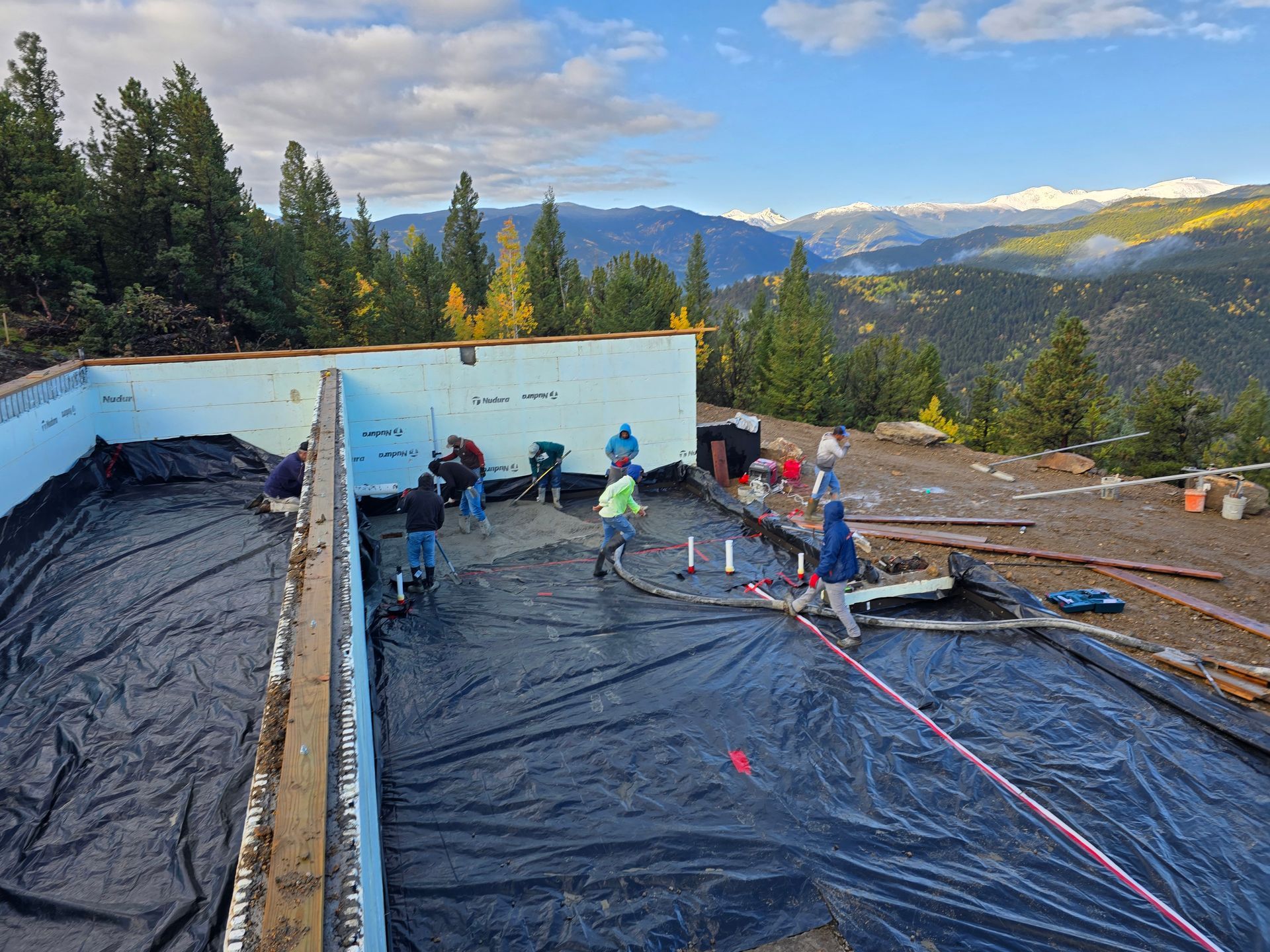 Workers on a roof membrane under construction, with mountains and trees in the background.