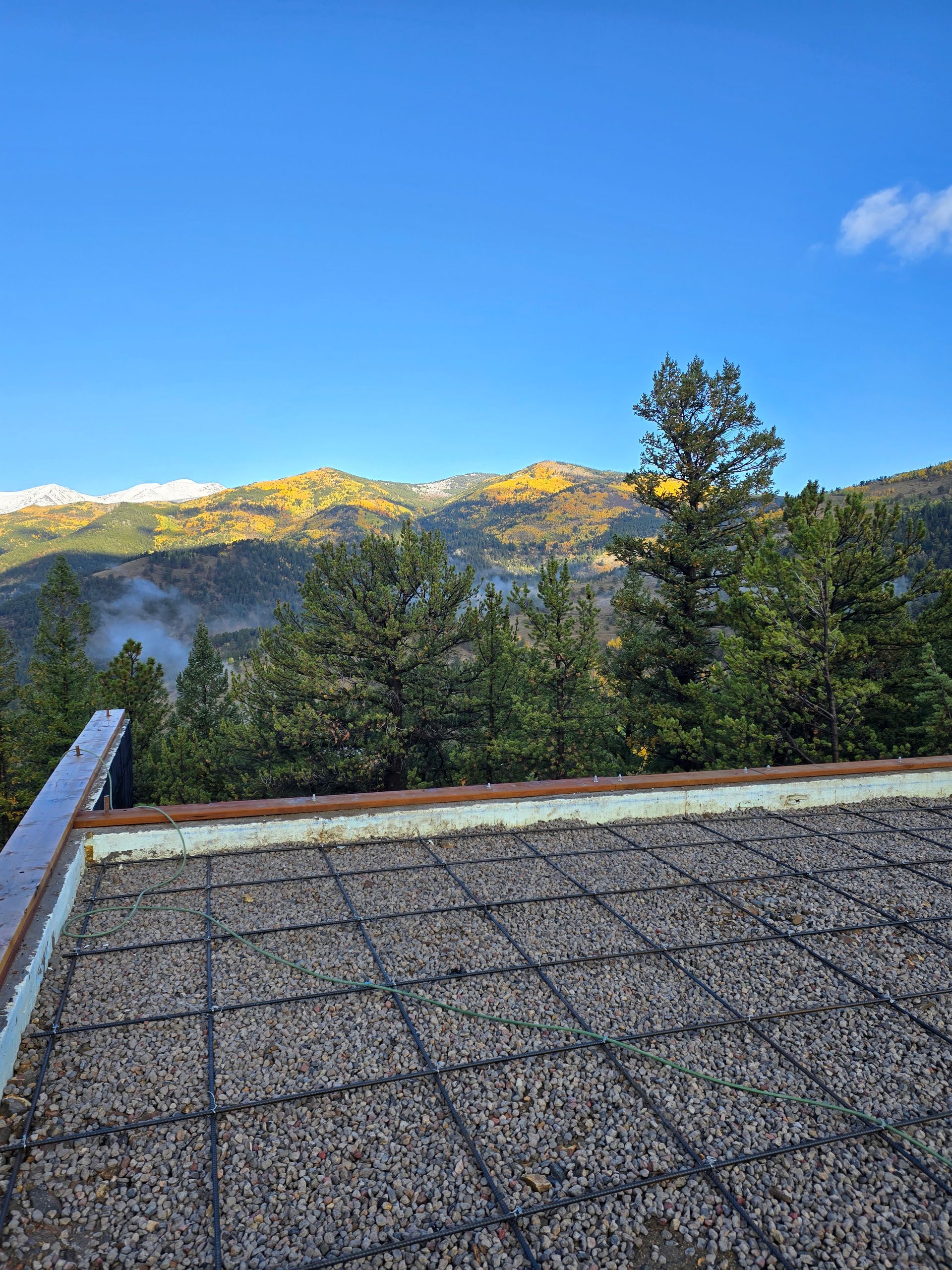 Rooftop with gravel surface overlooking pine trees, mountains, and a clear blue sky at sunrise