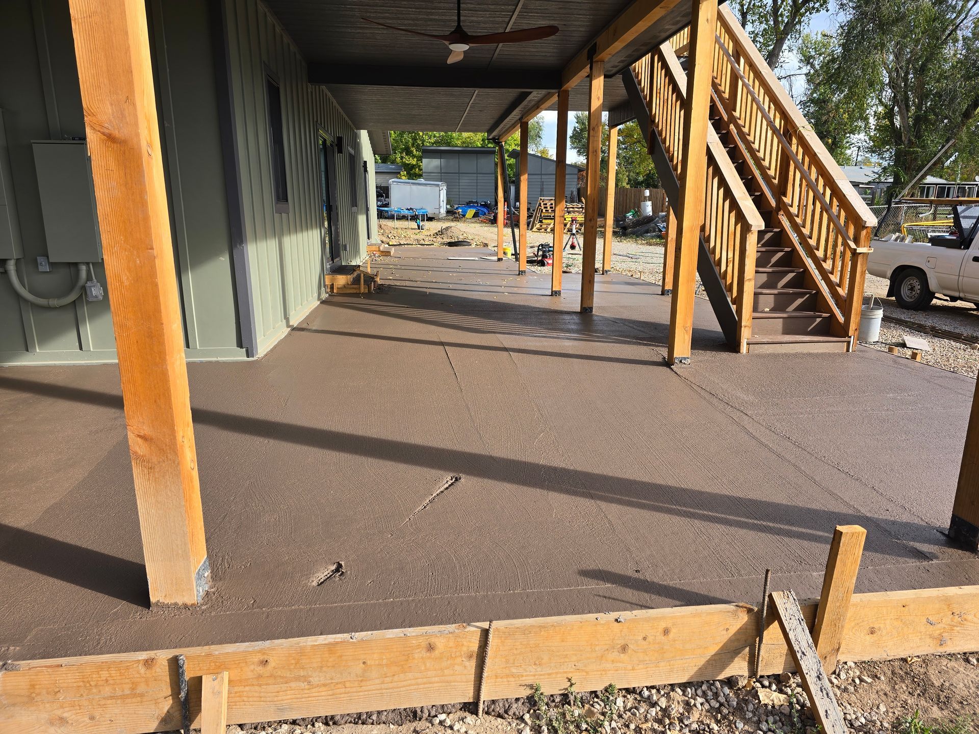 Covered outdoor walkway with wooden posts, stairs, and a concrete floor at a building exterior