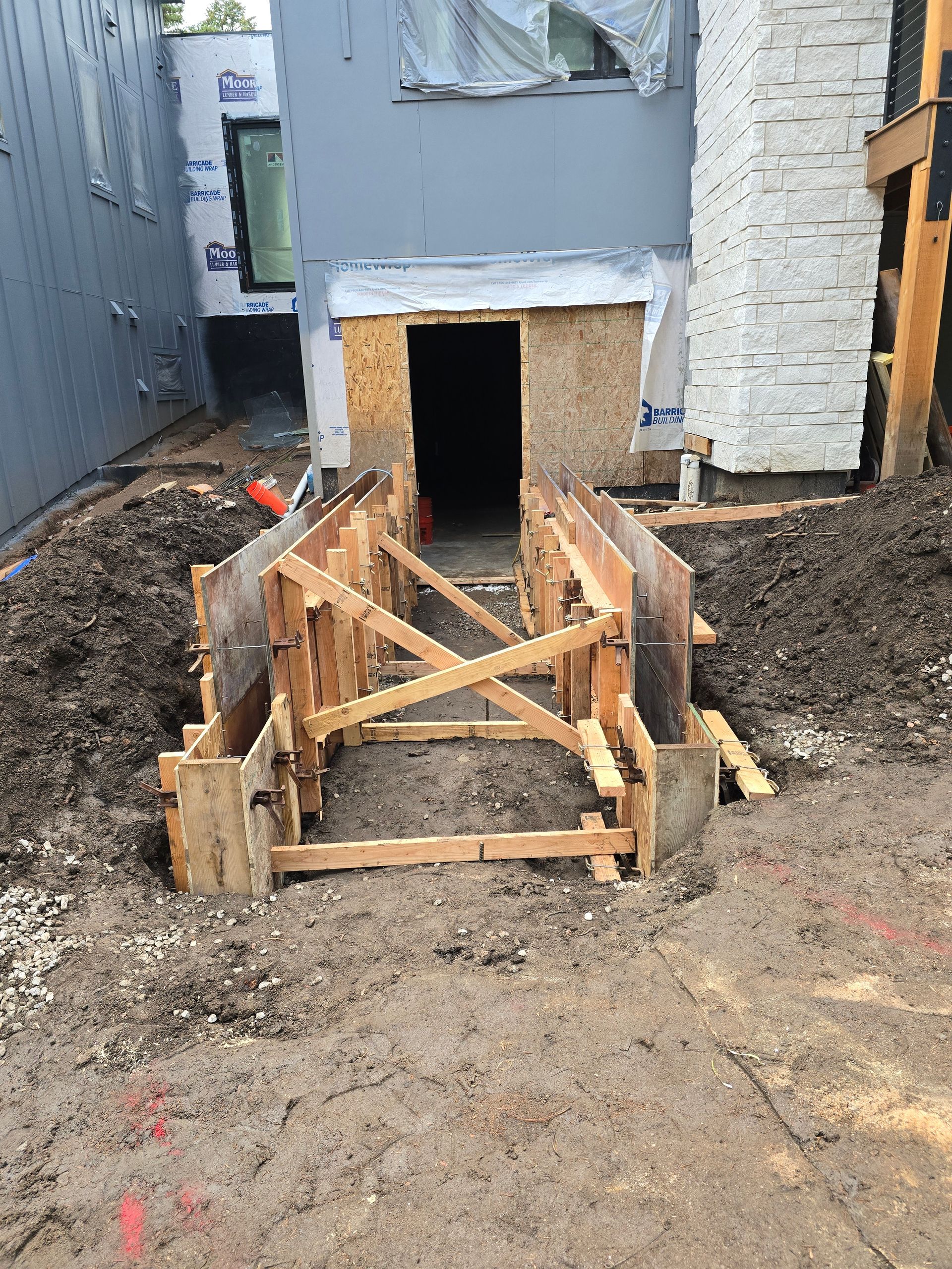 Wooden formwork framing a basement entrance at a construction site, surrounded by dirt and gravel.