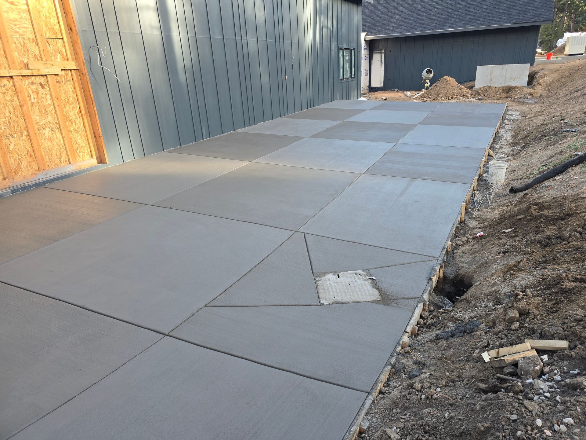 Concrete sidewalk slabs along a building beside a dirt slope and construction area