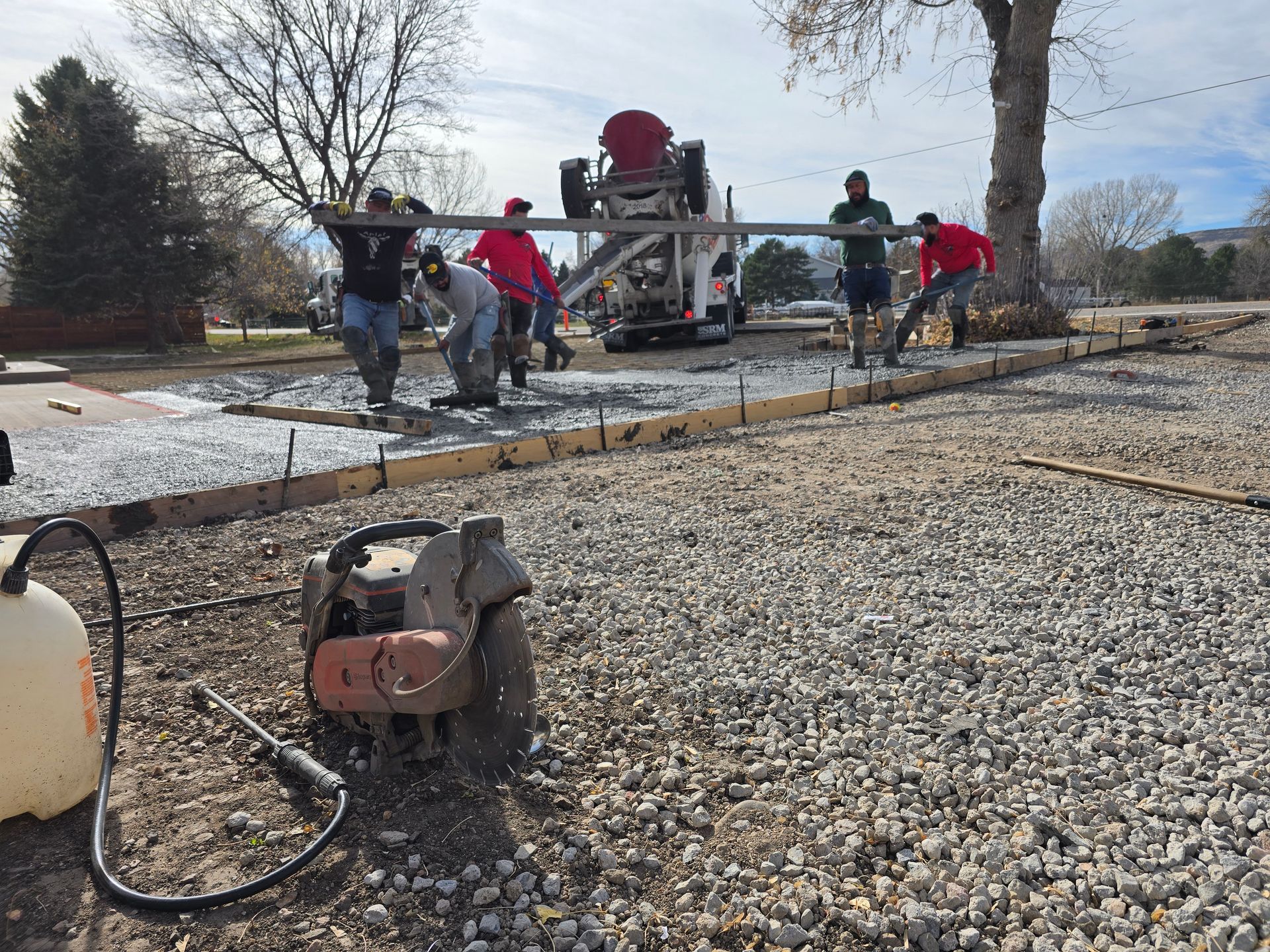 Workers using a concrete pump hose to pour a driveway slab on a gravel site