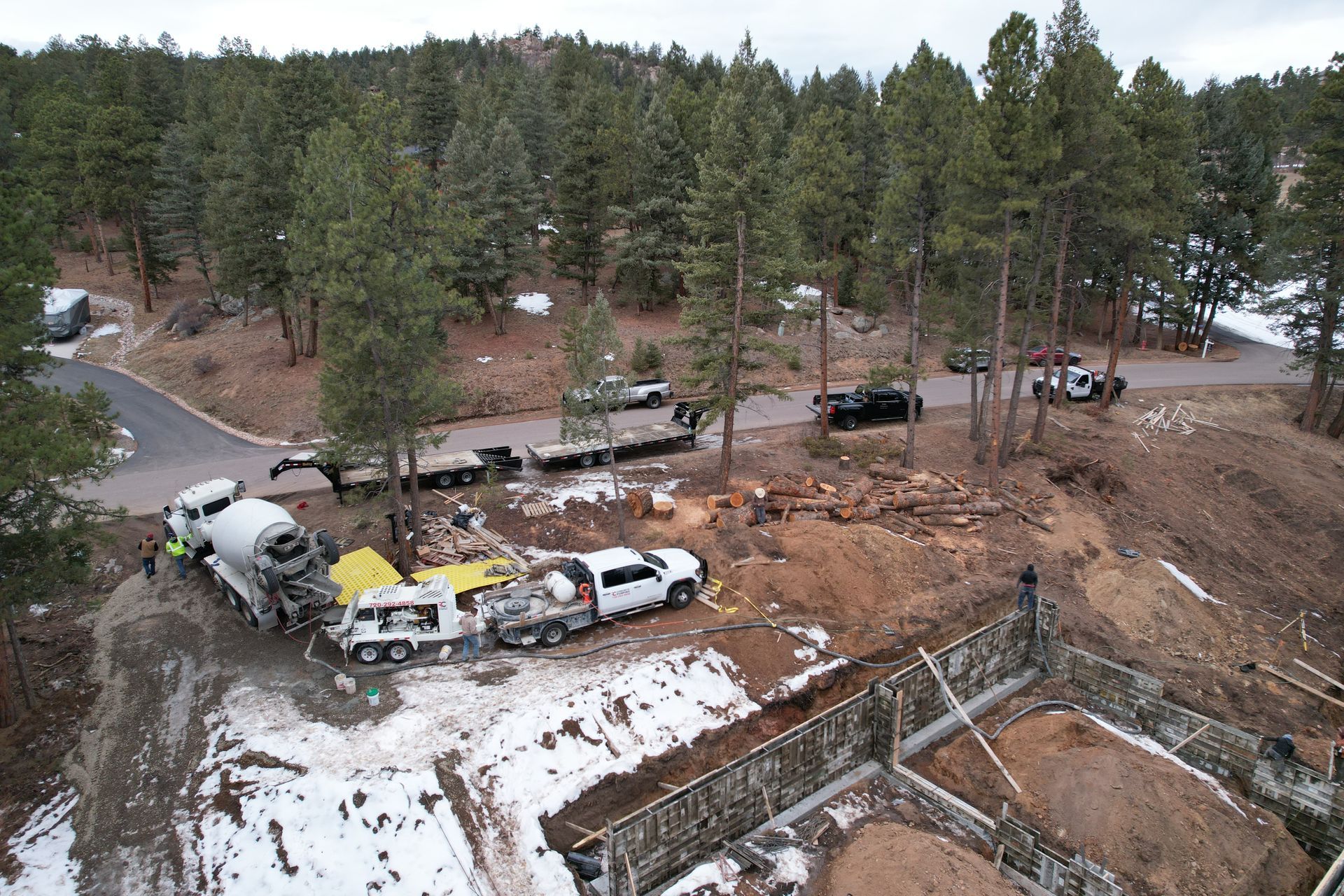 Overturned cement mixer and damaged vehicles at a snowy roadside construction site in a wooded area