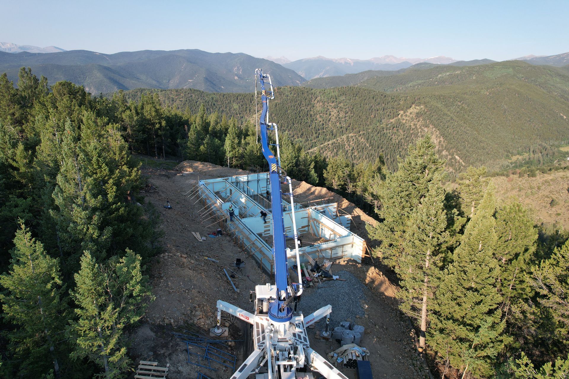 Construction crane on a wooded mountain slope with a road and distant hills under a clear sky