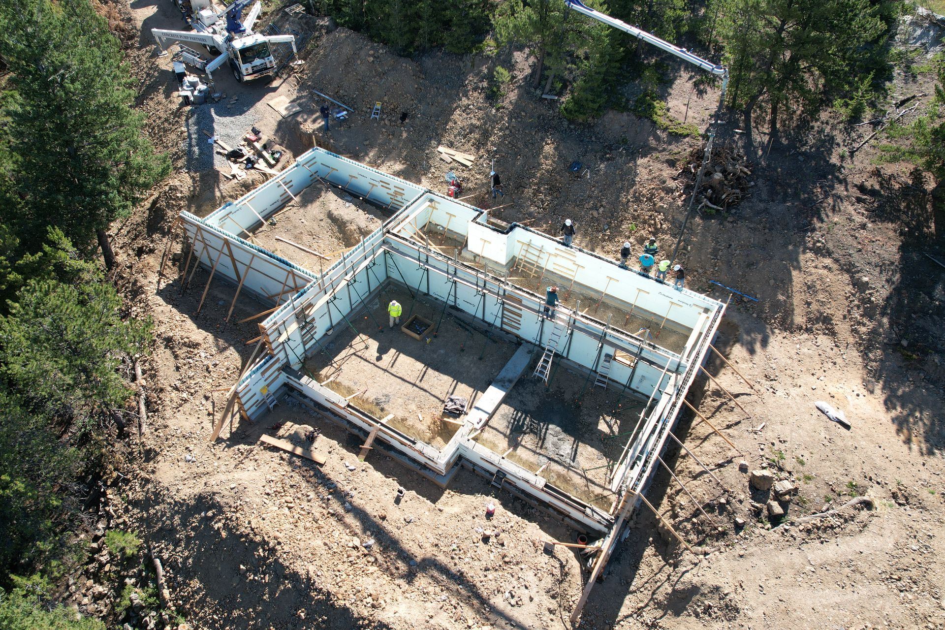 Aerial view of a foundation and basement walls under construction on a dirt lot.