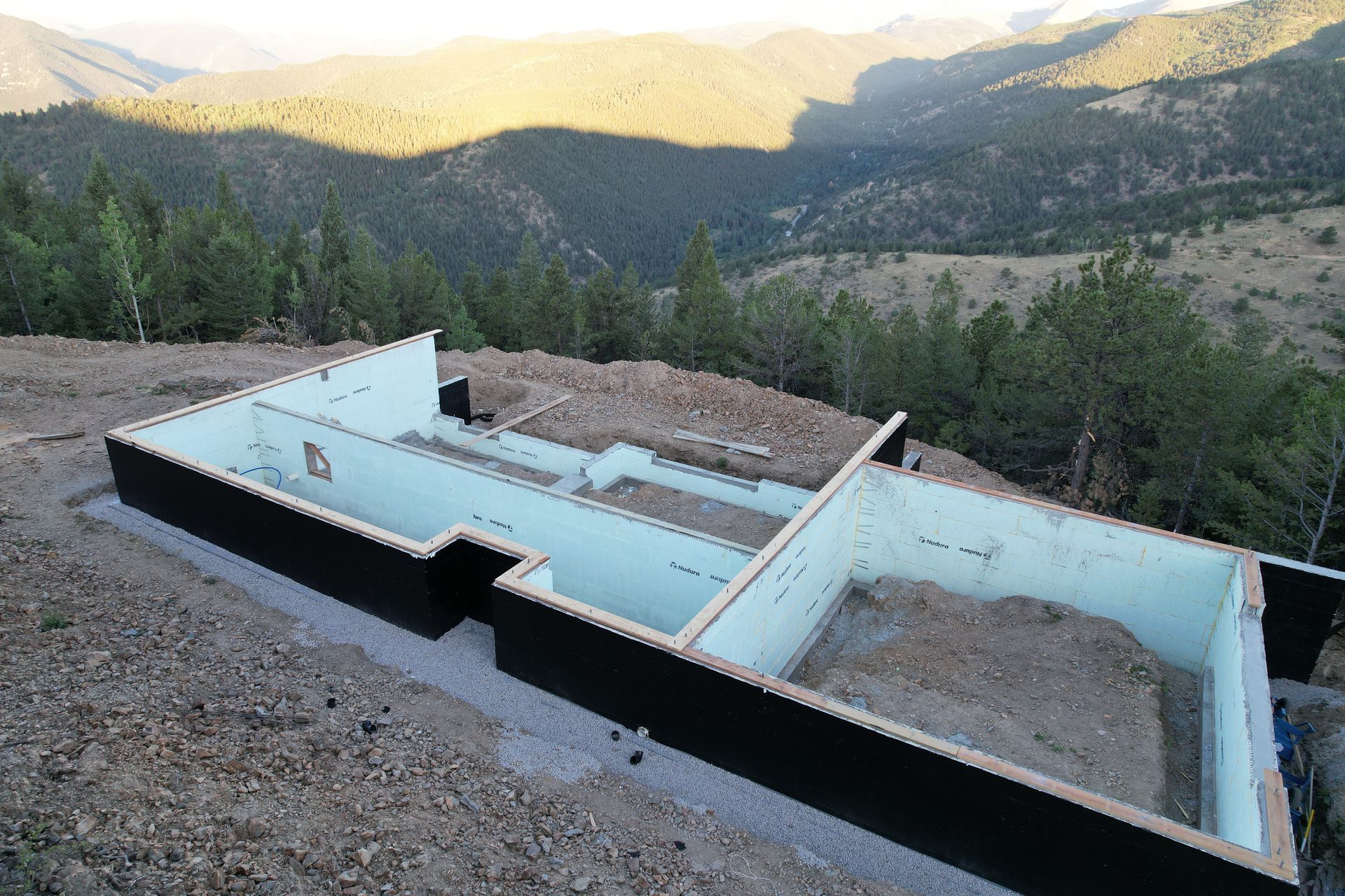Empty blue foundation or pool structure on a hillside overlooking a forested mountain valley at sunset