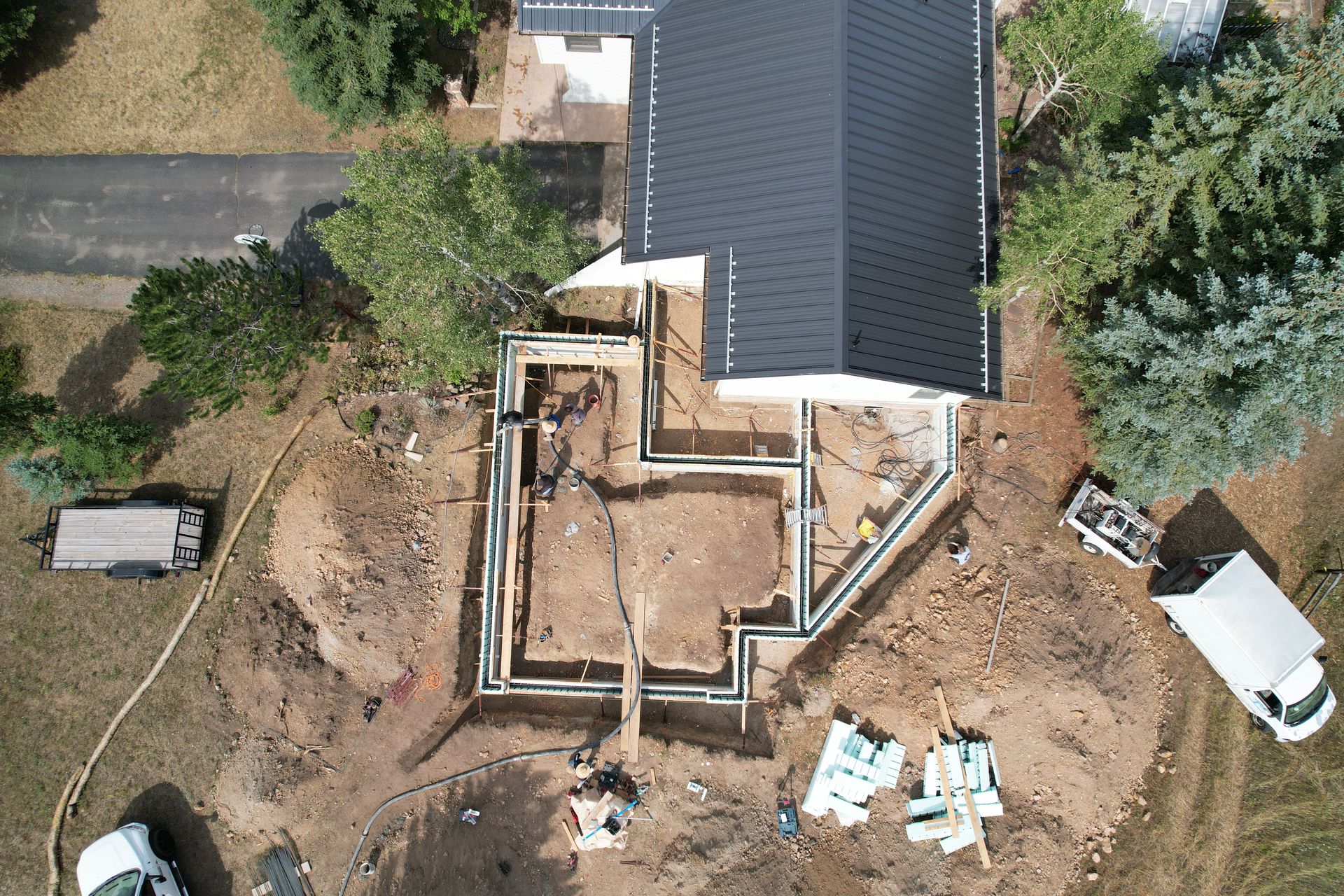 Aerial view of house construction with wooden foundation walls, dirt lot, and a white truck nearby.