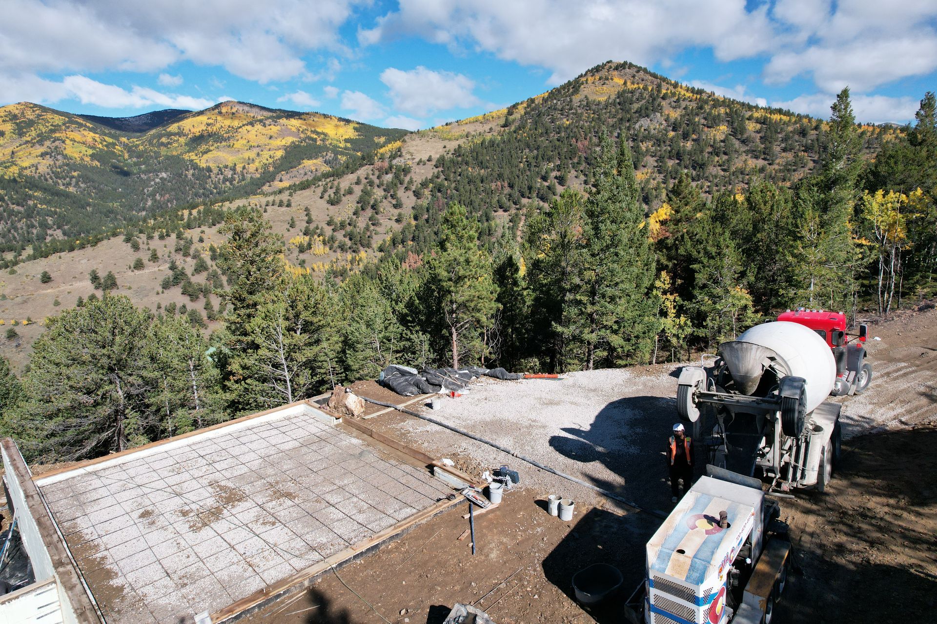 Mountain view with a roof under construction, workers’ equipment, and a cement mixer on a hillside.