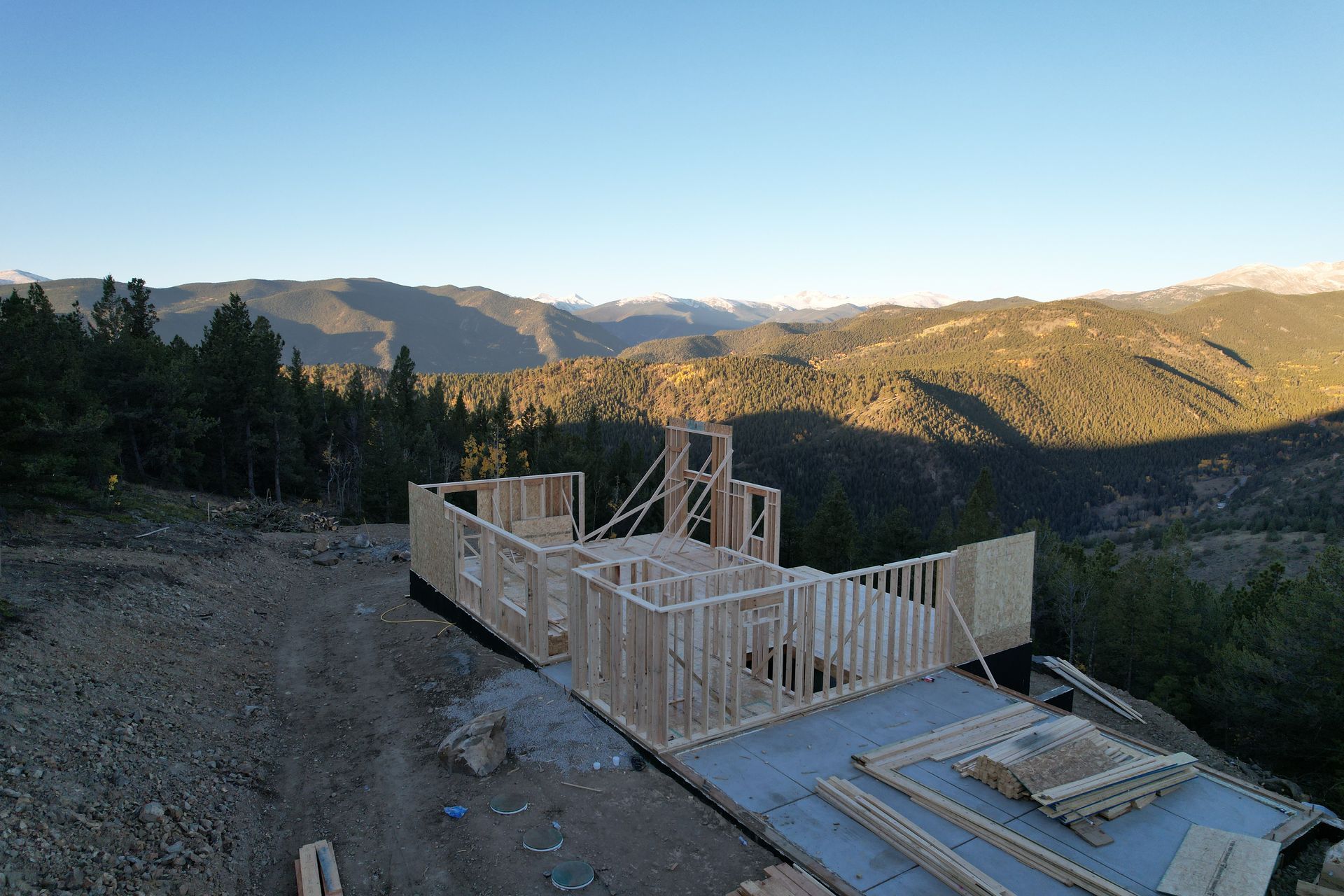 Wood-framed house under construction on a hillside with forested mountains in the background