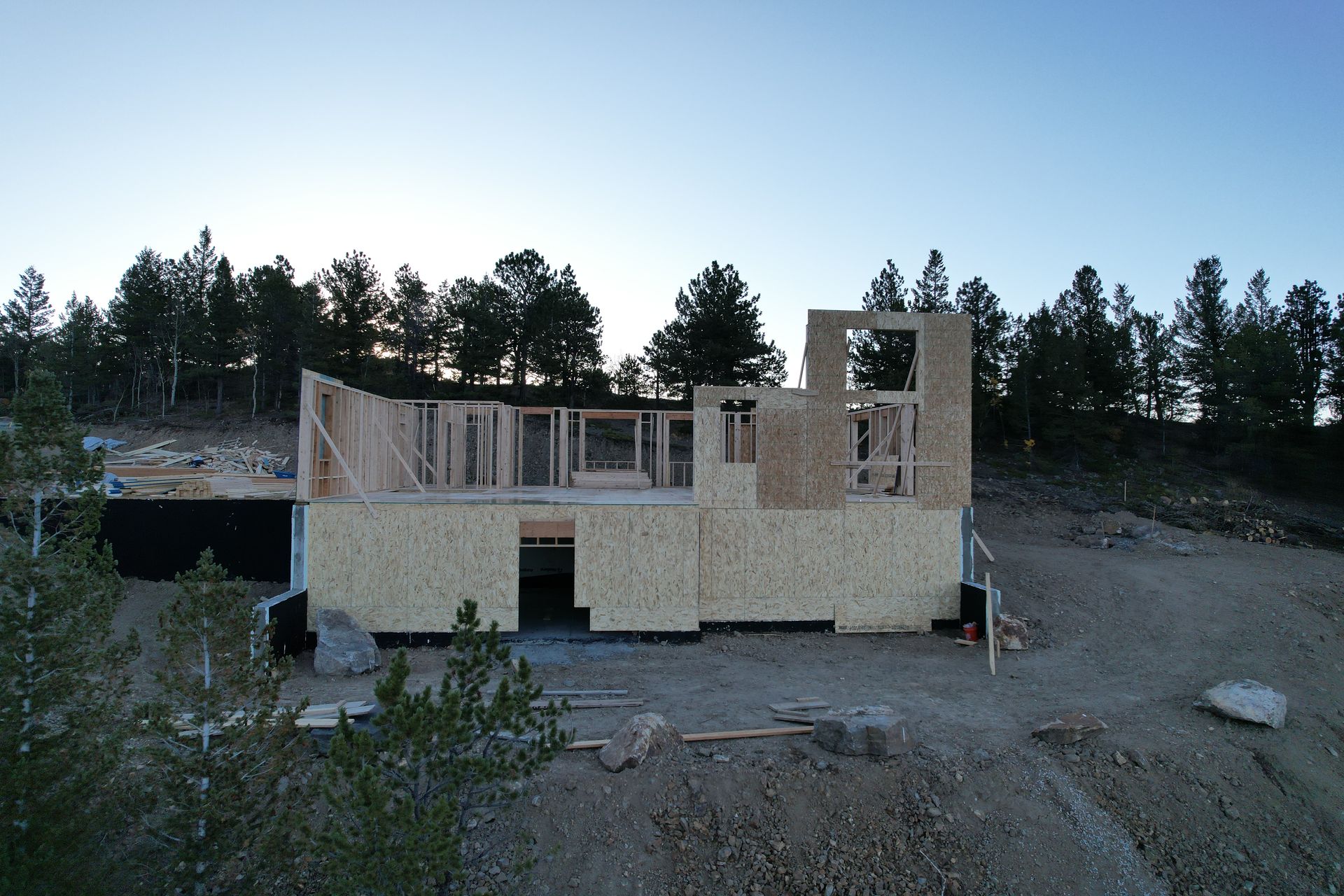 Partially built house in a wooded area at dusk, with exposed framing and unfinished walls.