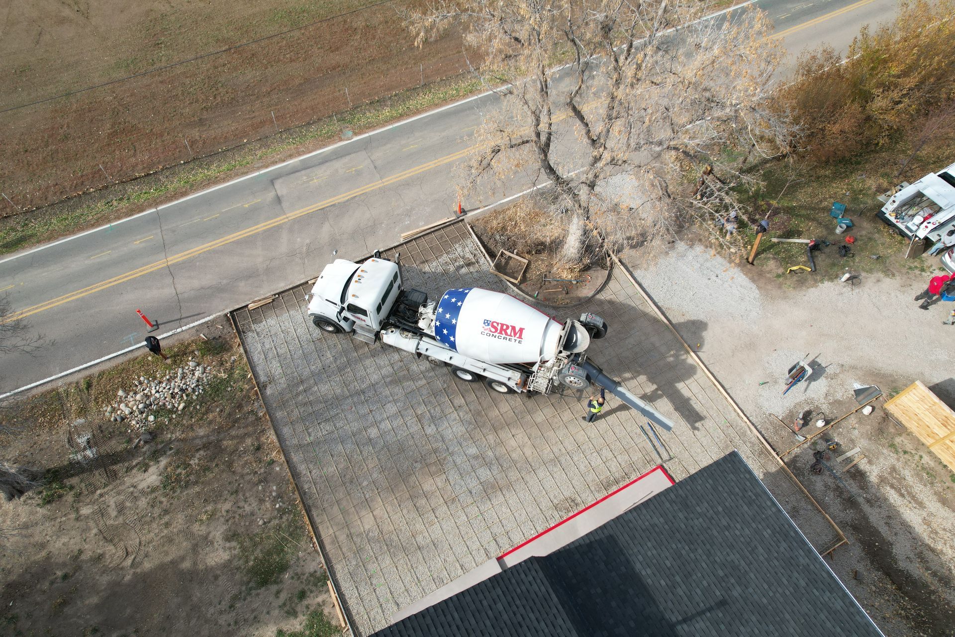 Aerial view of a white cement mixer truck parked by a roadside near a building and tree.