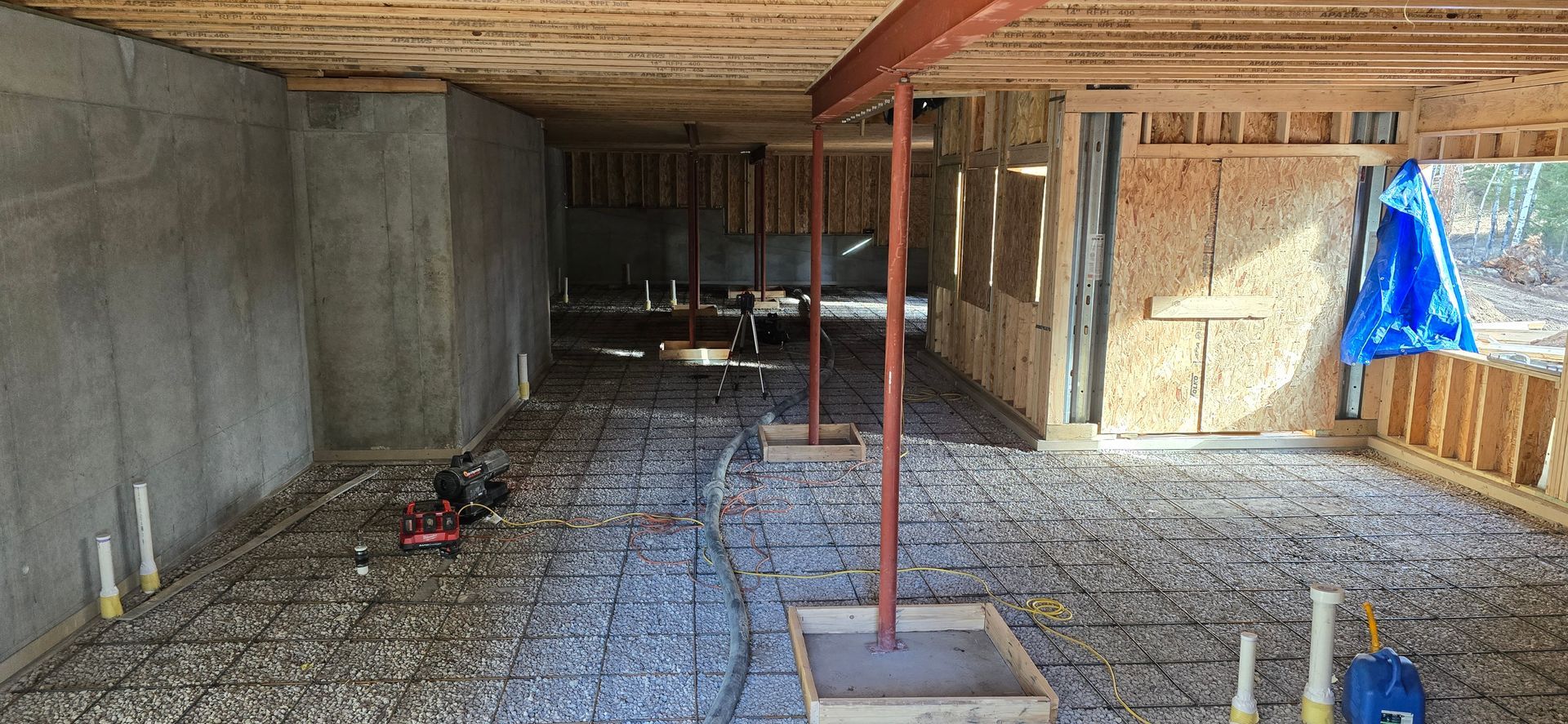 Unfinished basement interior with concrete walls, exposed studs, gravel floor, and construction materials.