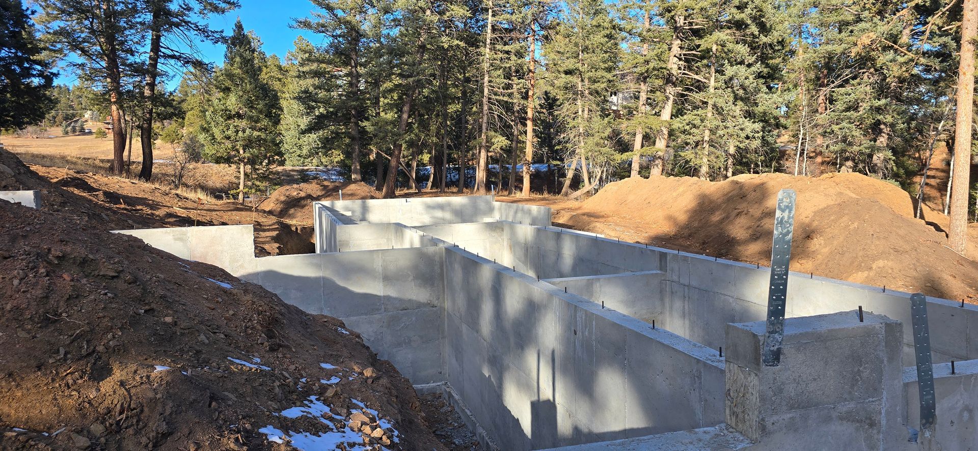 Concrete foundation walls at a construction site surrounded by dirt and pine trees