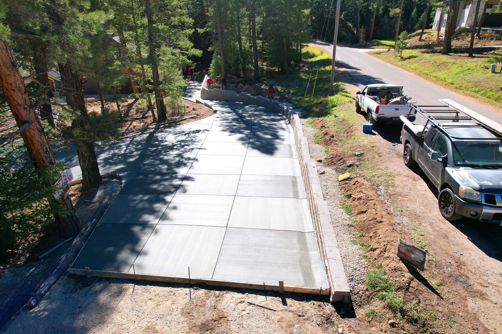 A newly paved driveway beside parked pickup trucks in a wooded area.
