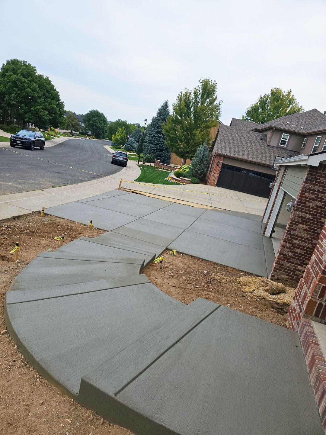 Curved concrete sidewalk and driveway beside suburban homes and a brick house on a sloped street