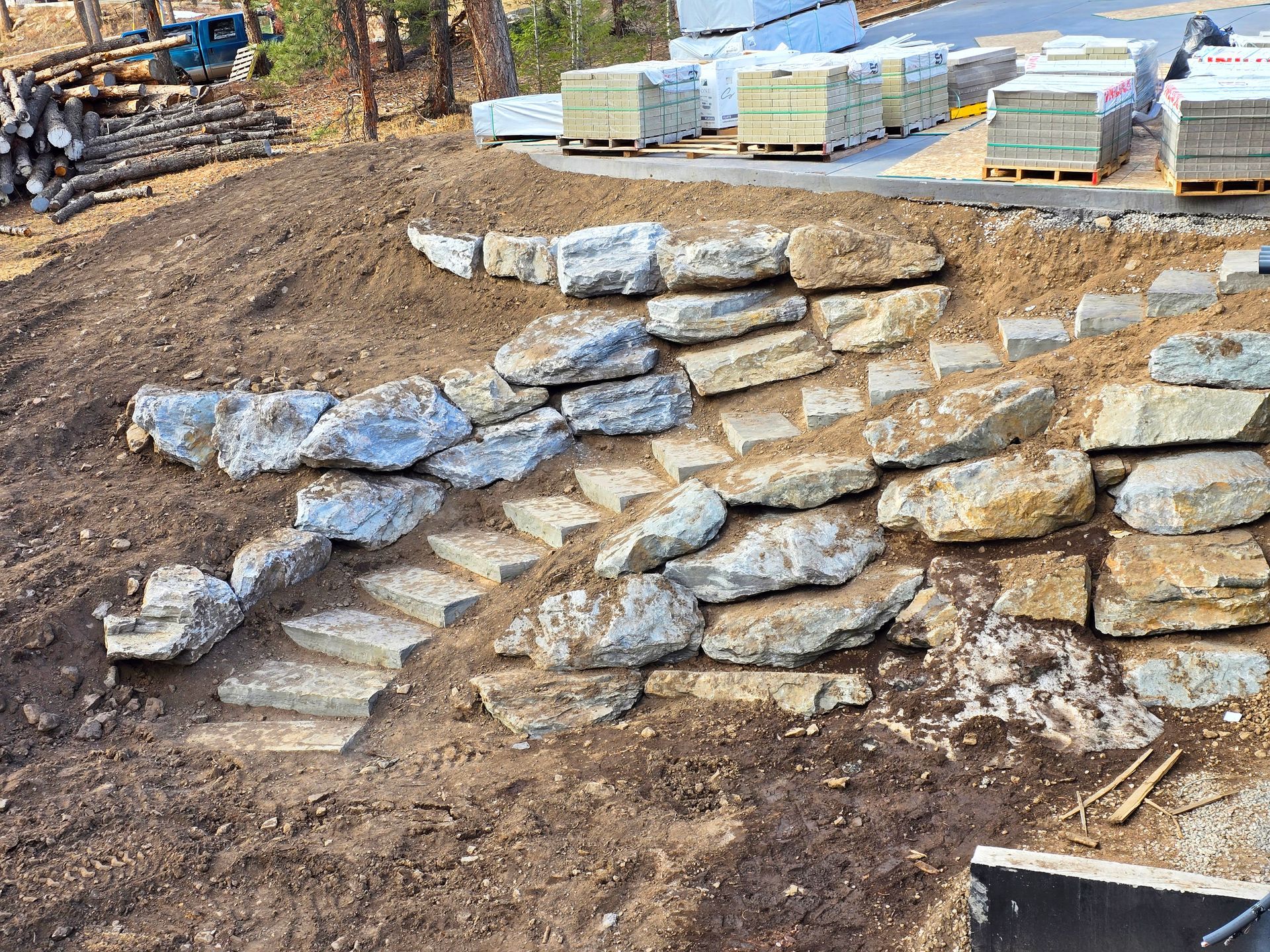 Stone retaining wall and steps built into a dirt hillside at a construction site.