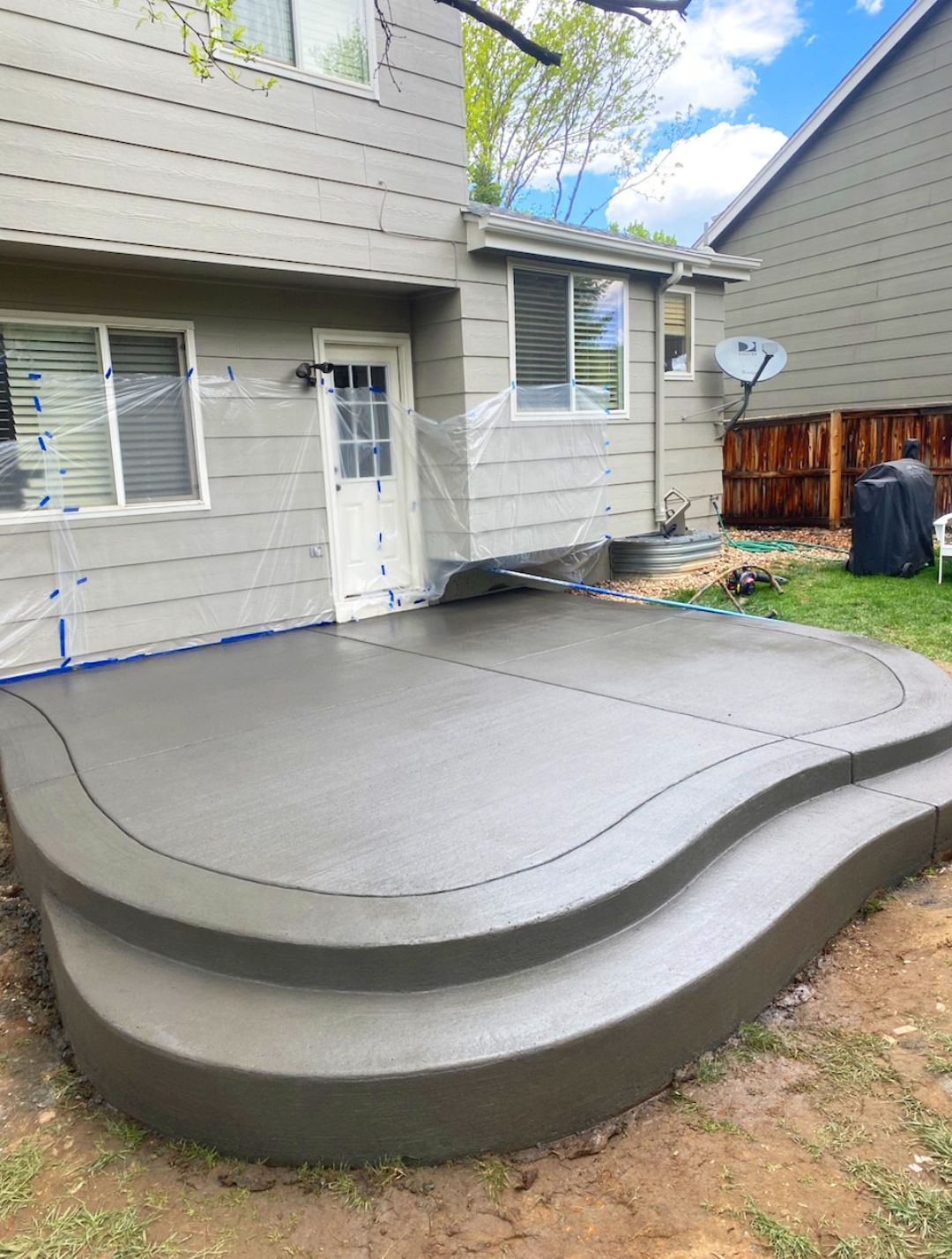 Backyard concrete patio with curved steps beside a house and wooden fence