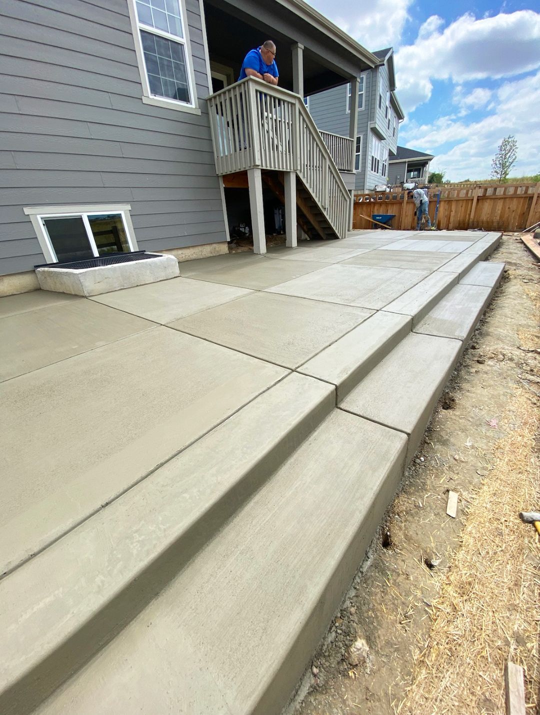 New concrete patio and steps beside a gray house under construction