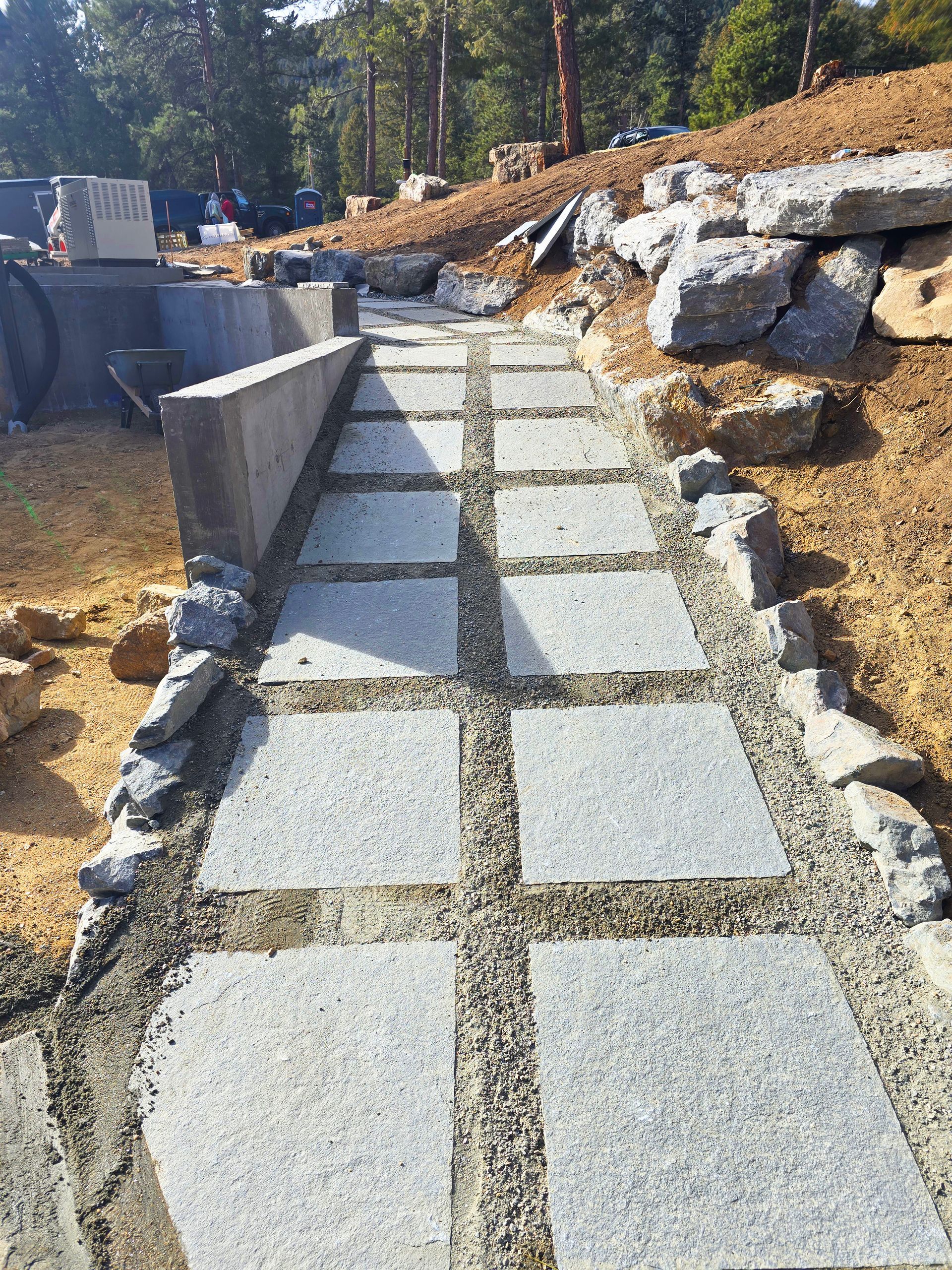 Stone walkway with a low retaining wall, leading uphill through a landscaped outdoor area.