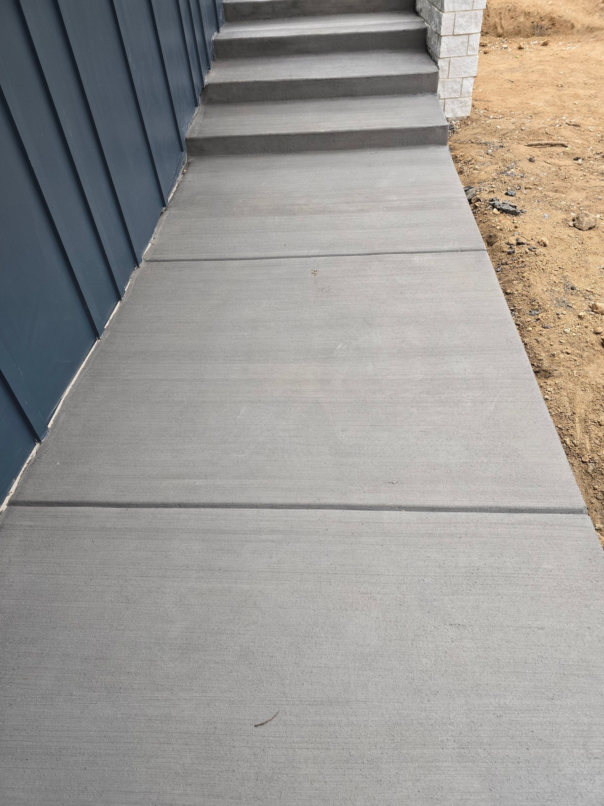 Concrete sidewalk beside a blue building, leading to steps with gravel on the right.