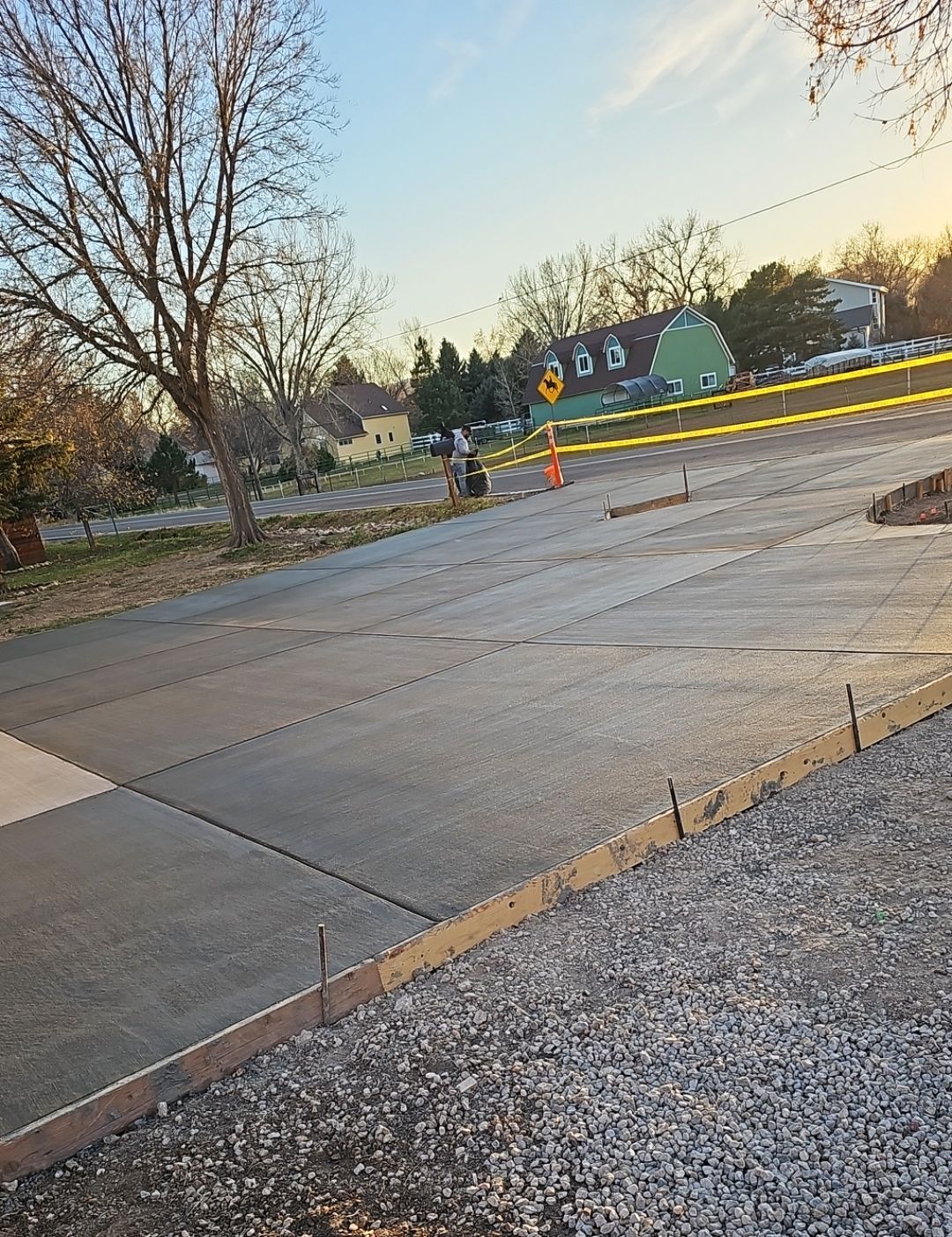 Empty paved lot beside trees at sunset, with yellow caution tape and a small traffic cone.
