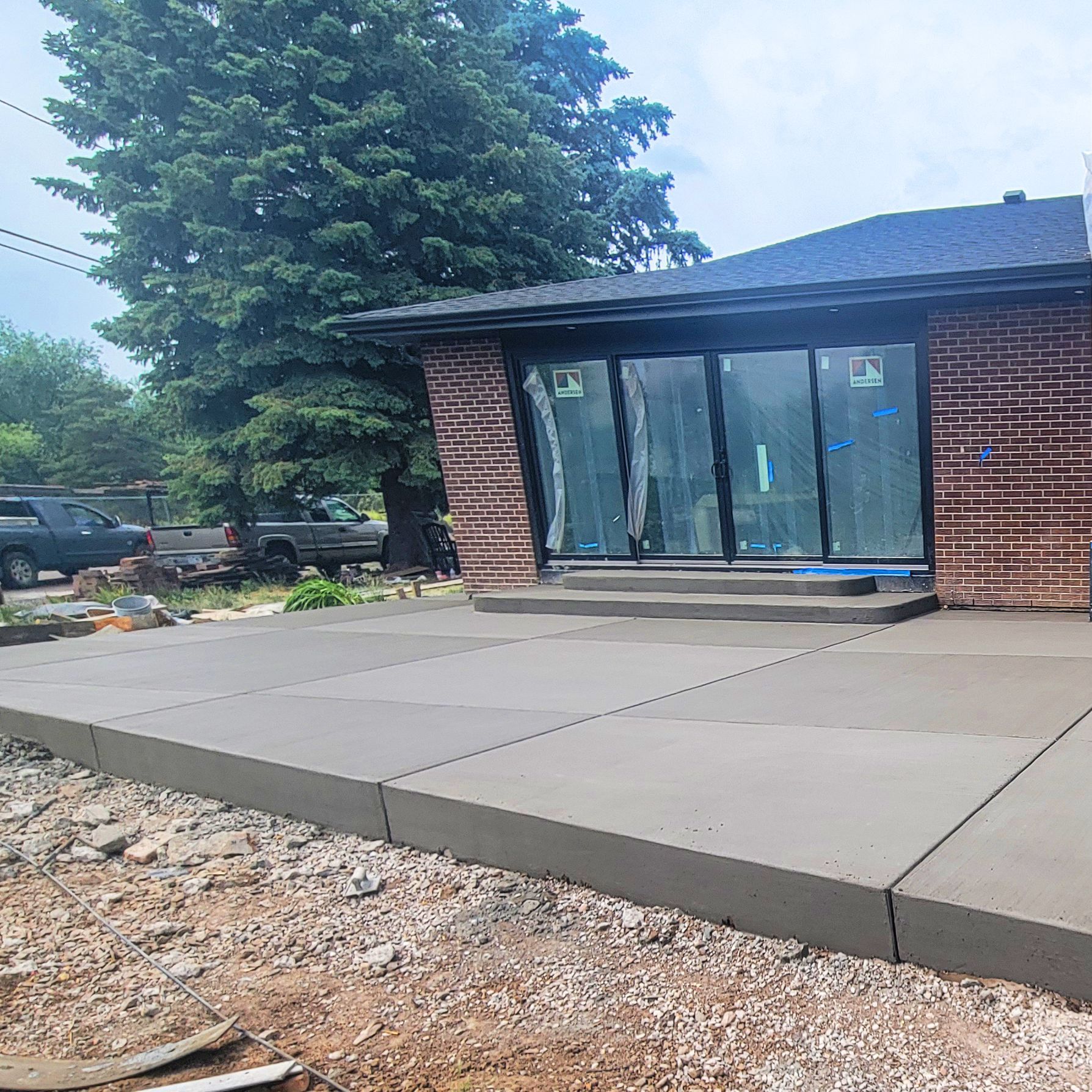 Front entrance of a brick building with a concrete walkway and large evergreen tree nearby