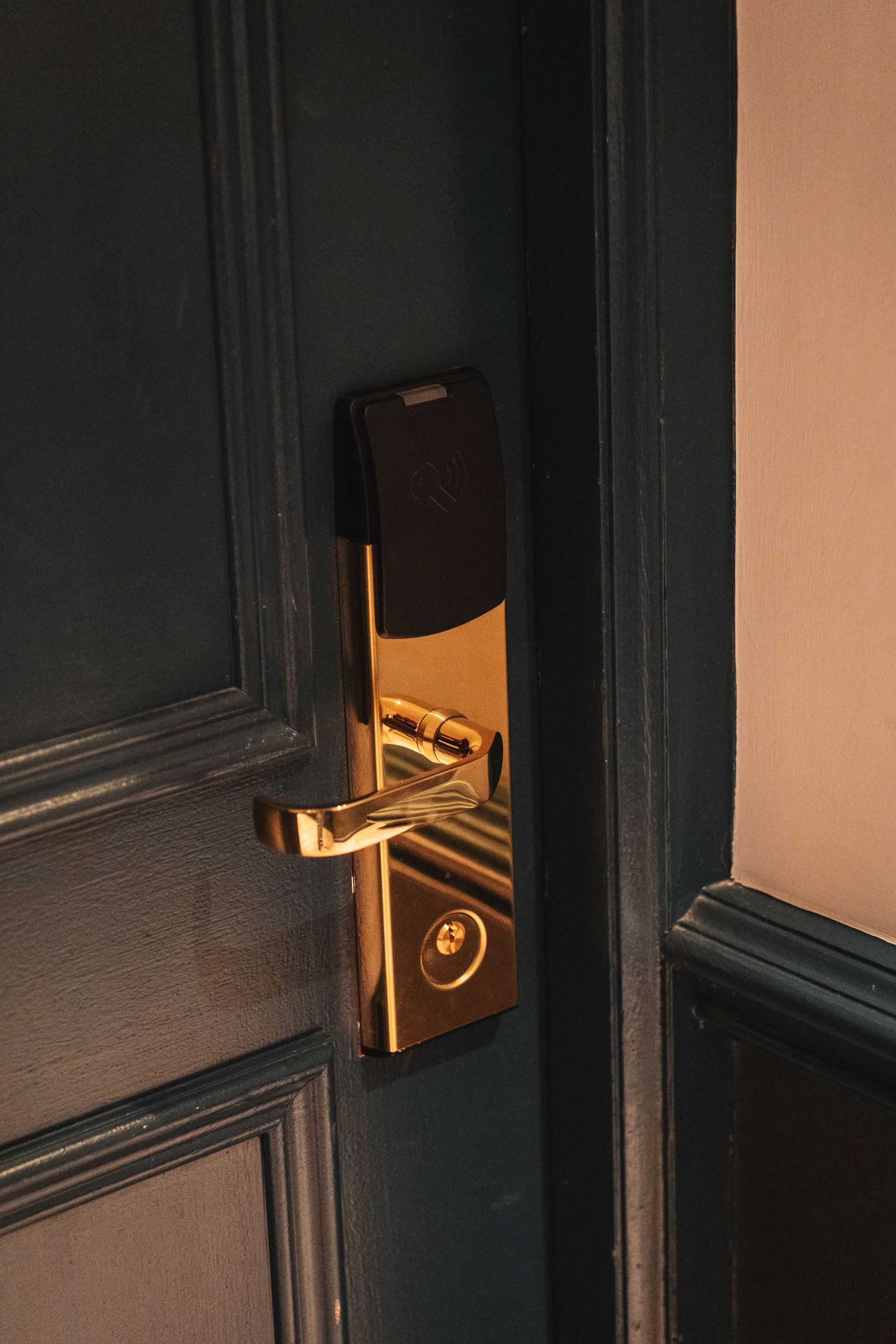 Gold hotel room door handle on a dark paneled door, partly open with warm light visible inside