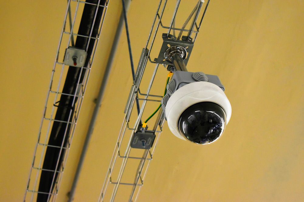 Ceiling-mounted security camera on a yellow industrial ceiling with metal support rails