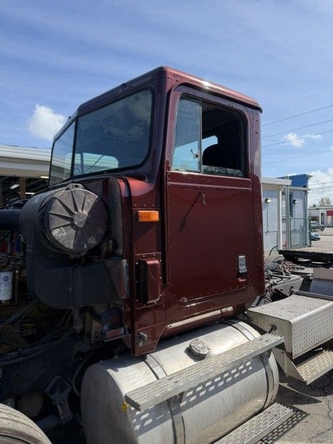 Maroon truck cab with a black spare tire on the side, parked outdoors under a blue sky.