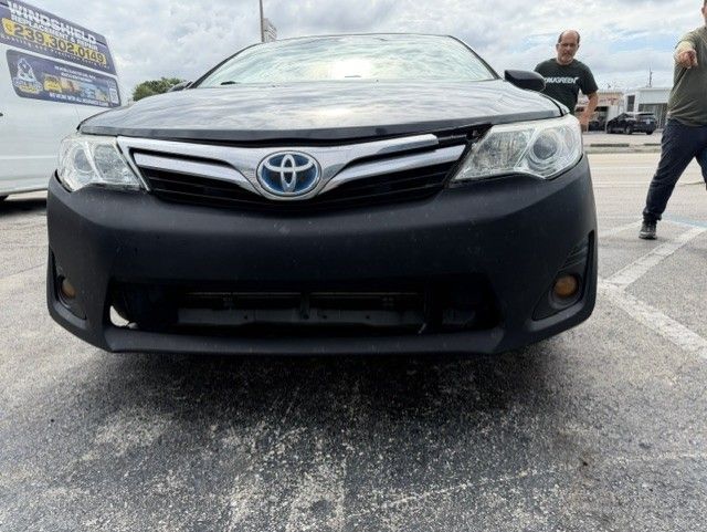 Front view of a black Toyota sedan parked in a lot, with a person standing in the background.