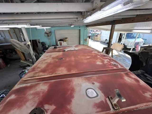 Rusty red car hood inside a garage with tools and equipment nearby