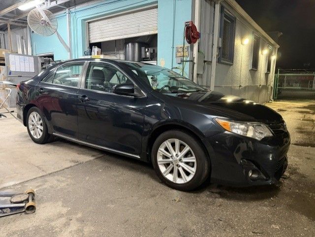 Black sedan parked outside an auto shop at night with visible front-end damage