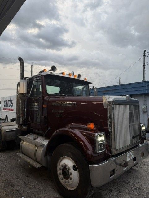 Maroon semi truck parked outdoors under cloudy sky, front view with chrome grille and white cab