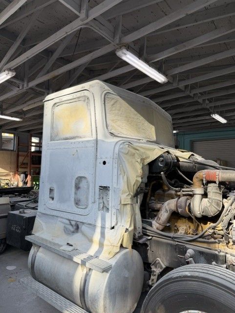 Dusty gray semi truck cab inside a warehouse, with exposed engine and large fuel tank.