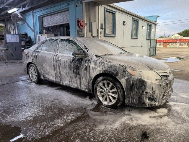Foam-covered sedan parked beside a car wash bay, with suds on the ground.