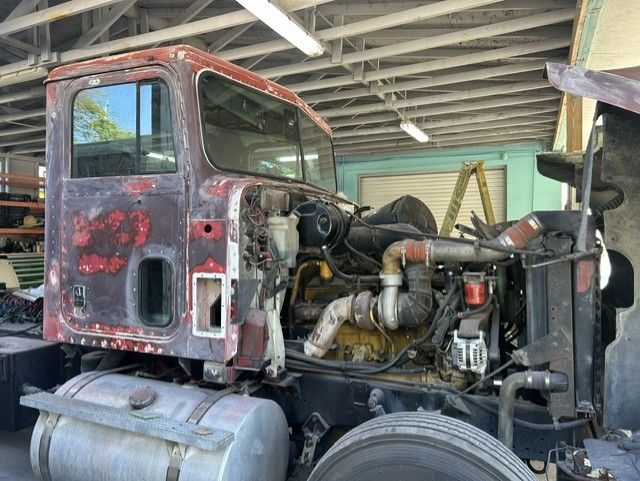 Old red semi truck cab under a shed, with exposed engine and frame, being repaired