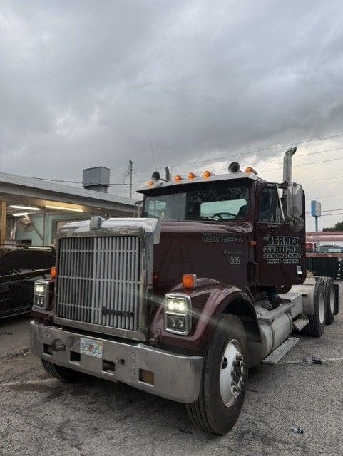 Maroon semi-truck parked under cloudy sky at a truck stop