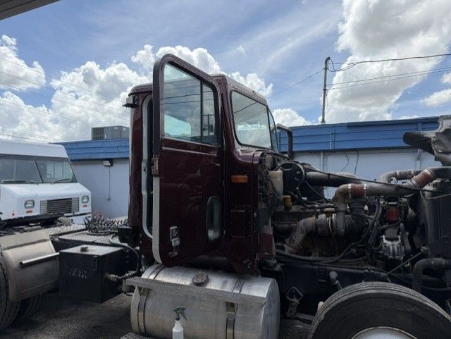Damaged semi-truck cab with open door and exposed engine in a truck yard