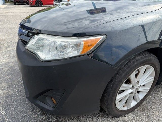Close-up of a dark gray car’s front-left side with a dented bumper and damaged headlight area.