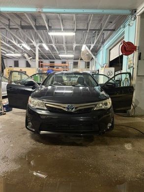 Black sedan in an auto shop with both front doors open and a wet floor under bright lights